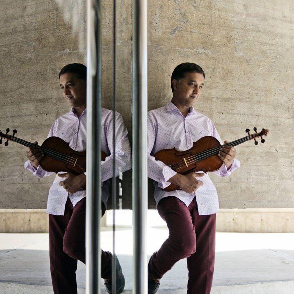 Ashan Pillai stands next to a mirror with a violin.