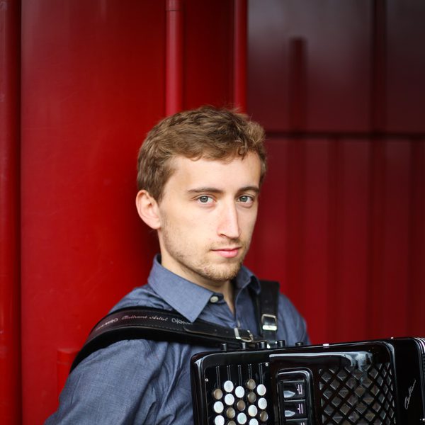Ben de Souza looks to camera, holding an accordion.