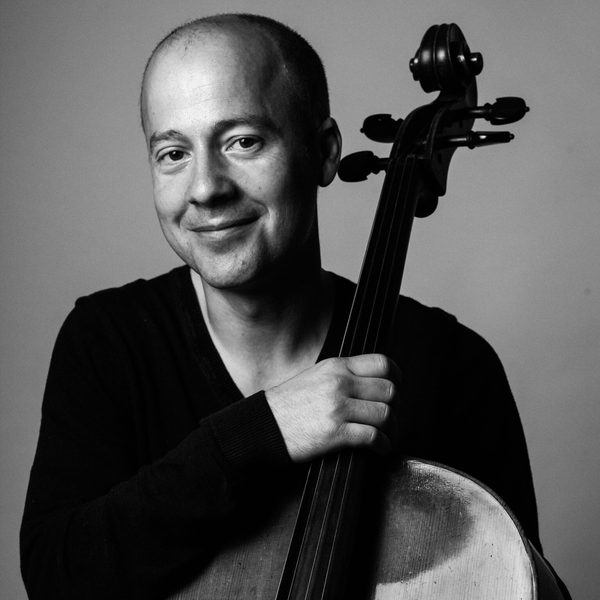 Black and white image of Boz Vukotic posing for headshot, holding cello.