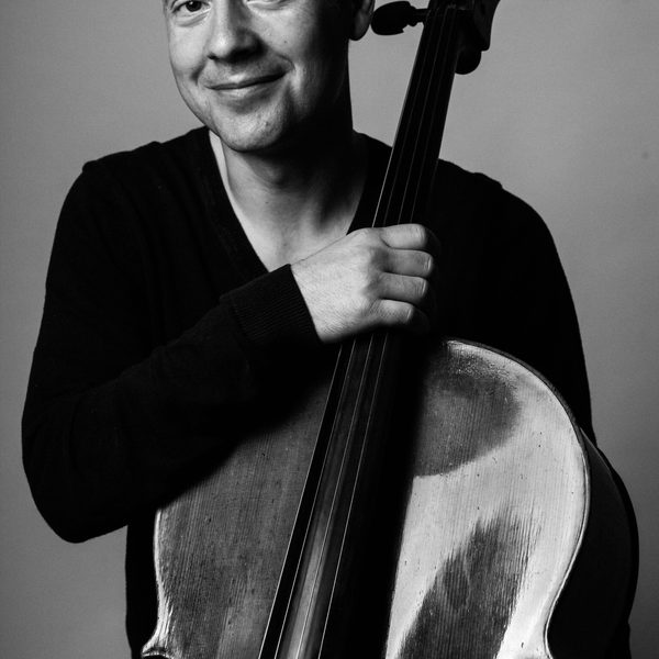 Black and white image of Boz Vukotic posing for headshot, holding cello.