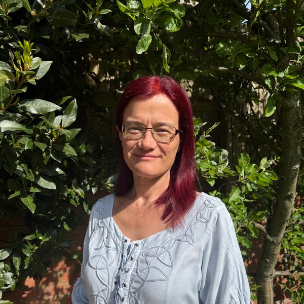 Briony Cox-Williams stands in a sunlit garden and looks to camera.