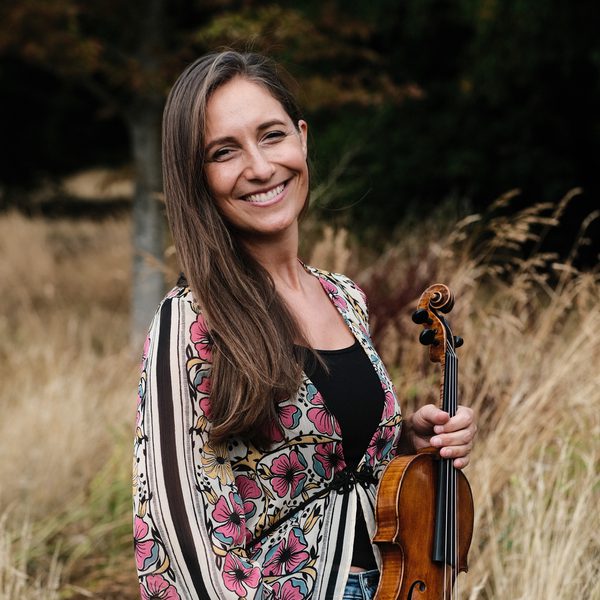 Portrait of Charis Jenson in a rural outdoor setting, holding a violin at waist height.