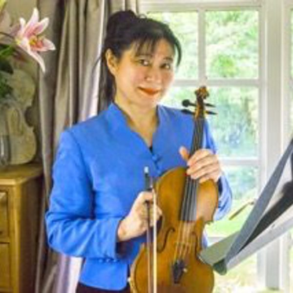 Chika Robertson poses for headshot indoors, standing with violin in hand at a music stand.