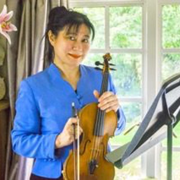 Chika Robertson poses for headshot indoors, standing with violin in hand at a music stand