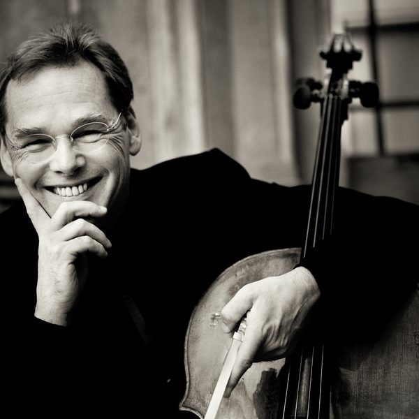 Christoph Richter smiles to camera, supporting his face in his hand and hugging a cello