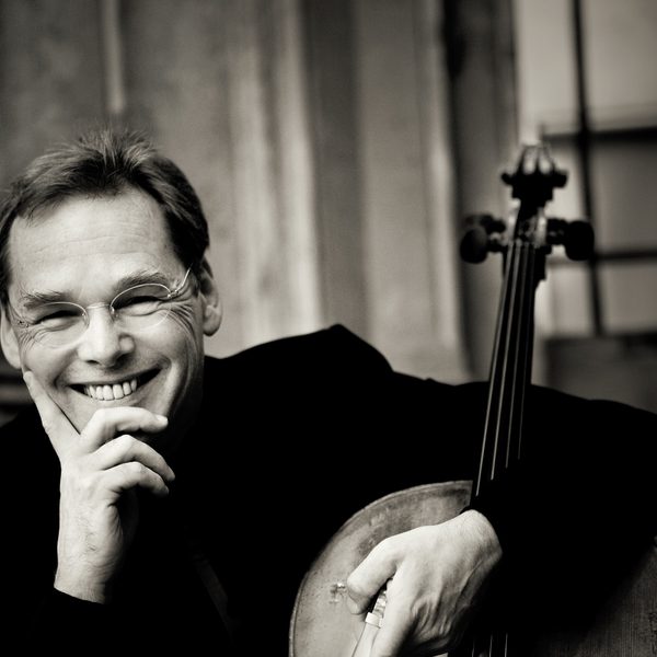Christoph Richter smiles to camera, supporting his face in his hand and hugging a cello.