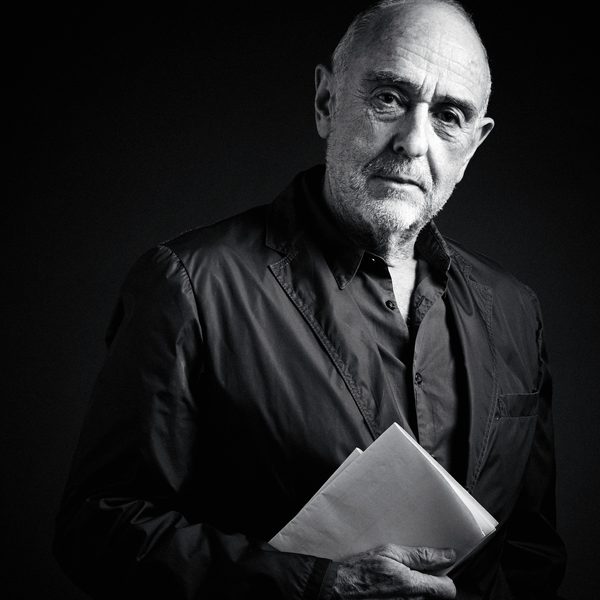 Black and white image of Claude Michael Shönberg posing against a black background, holding a playbook.