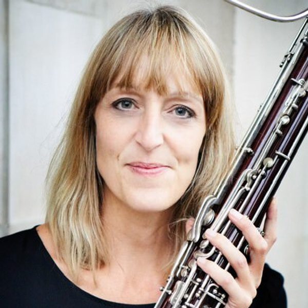 Connie Tanner holds a bassoon, facing camera, outside.