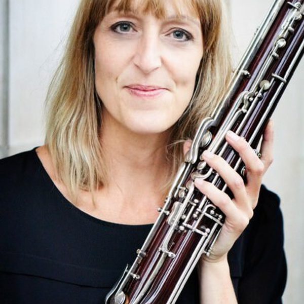 Connie Tanner holds a bassoon, facing camera, outside