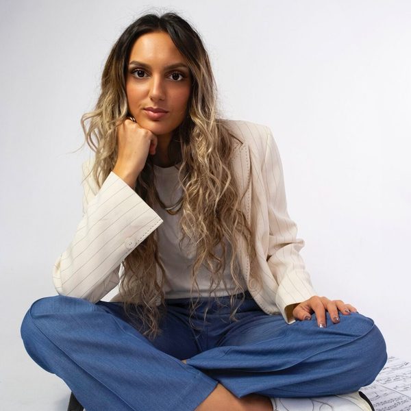 Crystalla Serghiou smiles to camera, sitting cross-legged on the floor on top of sheet music with head resting on fist.