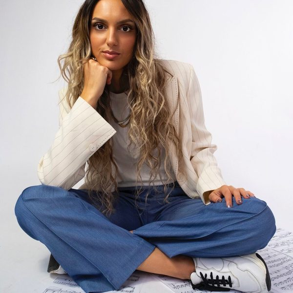 Crystalla Serghiou smiles to camera, sitting cross-legged on the floor on top of sheet music with head resting on fist
