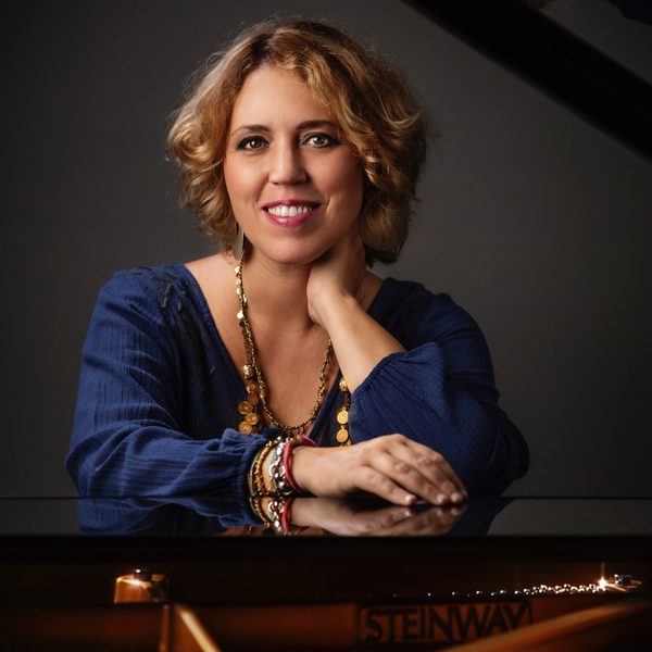 A woman smiles for camera, leaning across the top of a piano