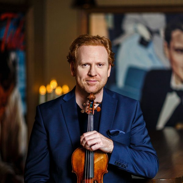 Daniel Hope poses for camera, holding a violin against his chest.