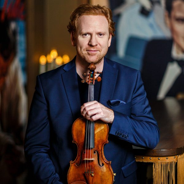 Daniel Hope poses for camera, holding a violin against his chest.