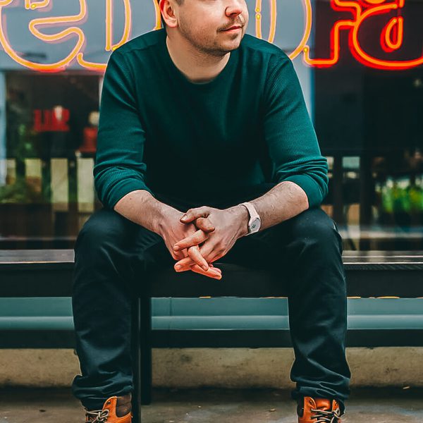 Portrait of David Taylor sitting outside on a bench, looking away from camera
