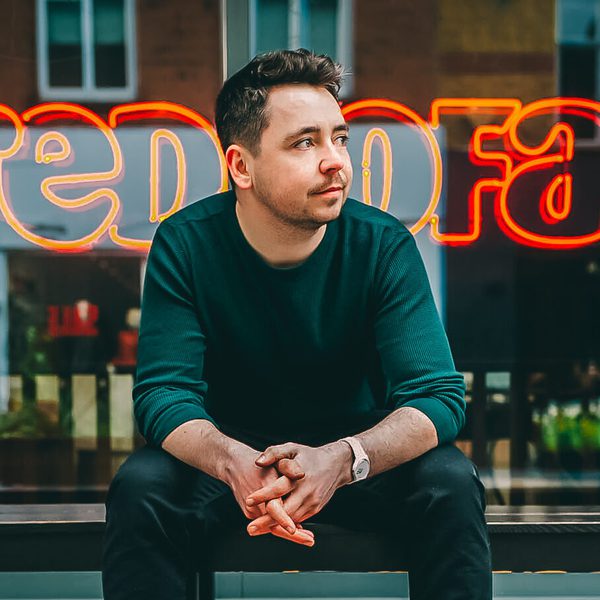 Portrait of David Taylor sitting outside on a bench, looking away from camera.