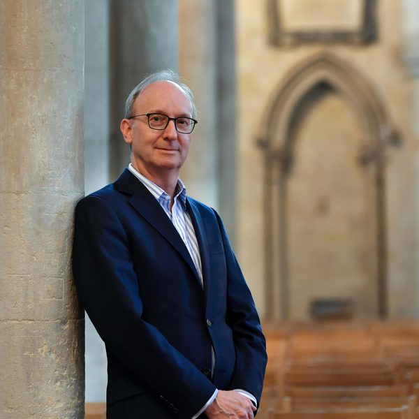 David Titterington smiles to camera with arms held in front, leaning against a church column.