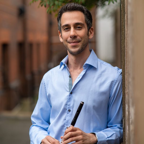Diomedes Demetriades holds a piccolo outside, leaning against a wall