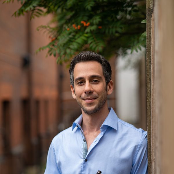 Diomedes Demetriades holds a piccolo outside, leaning against a wall.