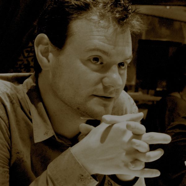 Close up of Dominic John, looking out of frame, clasping hands.