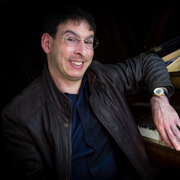 Duncan Honeybourne sits at a piano keyboard smiling.