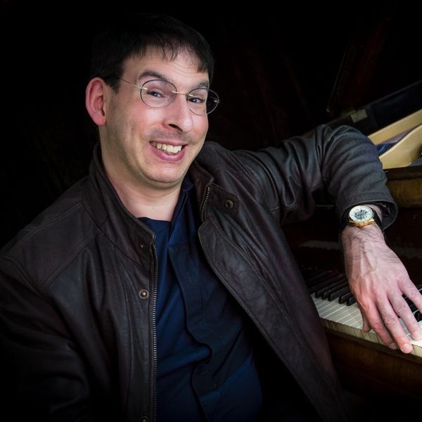 Duncan Honeybourne sits at a piano keyboard smiling