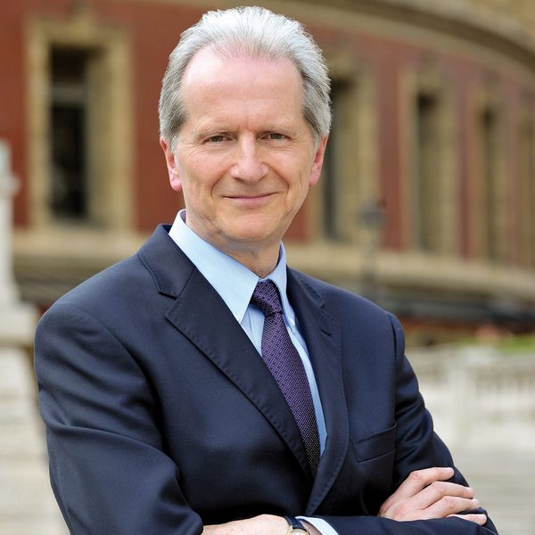 A man in a suit and tie standing with arms crossed in front of a building