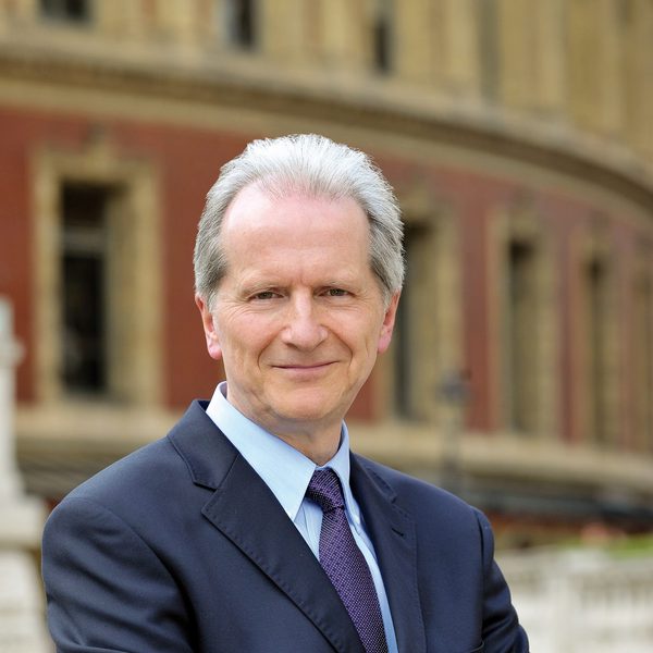 A man in a suit and tie standing with arms crossed in front of a building.