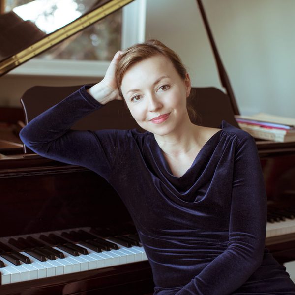 Elena Langer smiles to camera, sat at a piano.