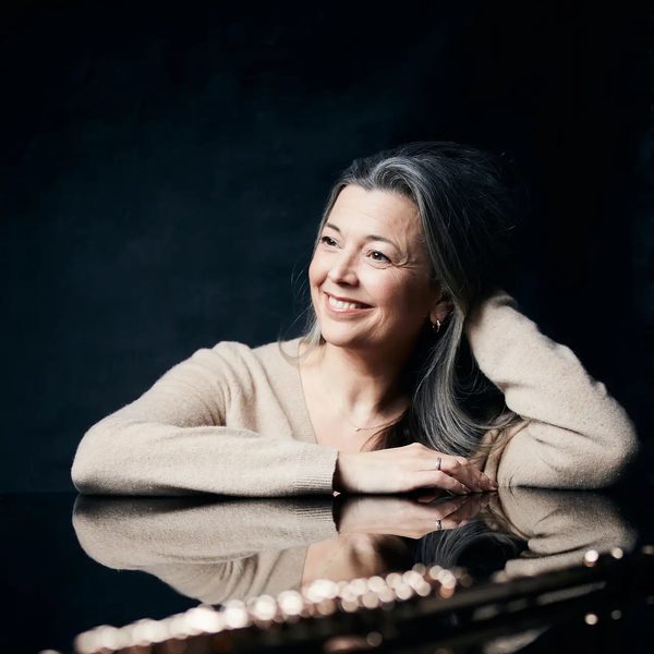 Emily Beynon sits at a table in a dark room, with flute in the foreground.