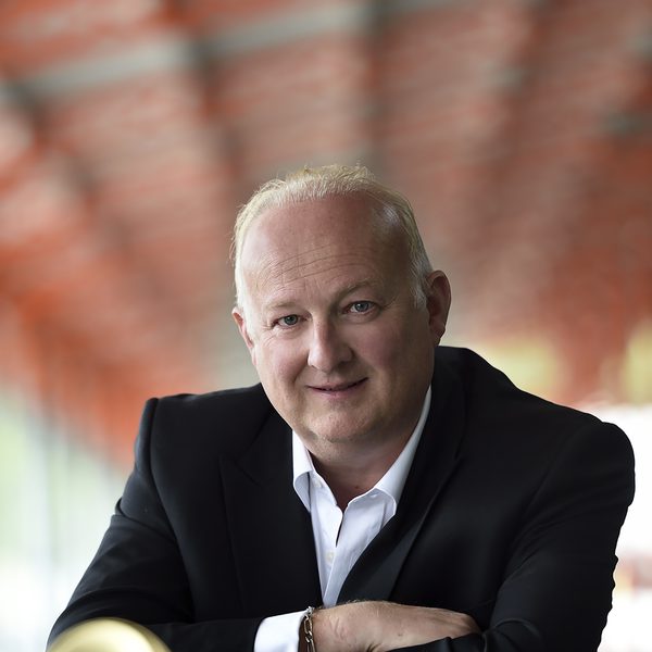 Eric Aubier looks to camera with arms folded, with his trumpet lying on the table in front of him.