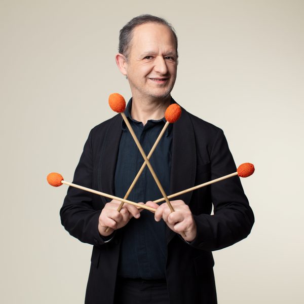 Eric Sammut smiles to camera while holding four drum beaters in a pattern.