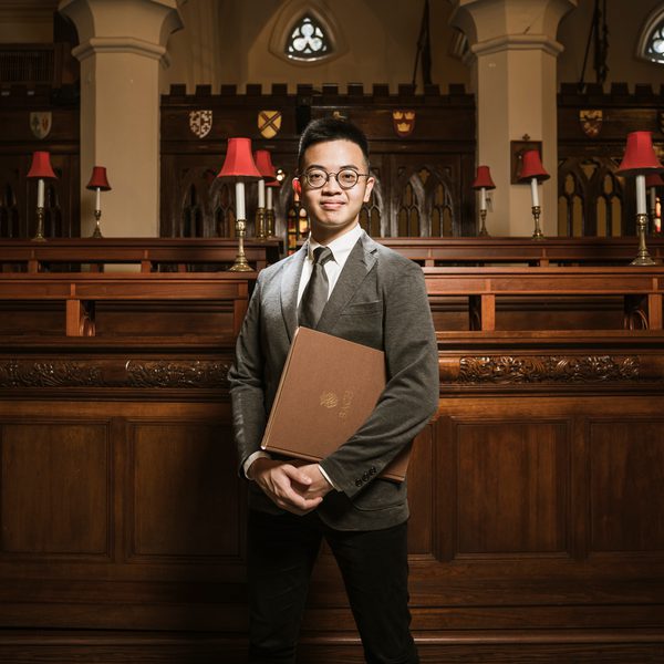 Felix Yeung smiles to camera, holding sheet music.