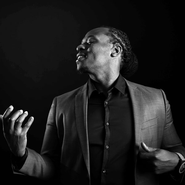 Femi Temowo poses as if with a guitar in his hands, lit from the side