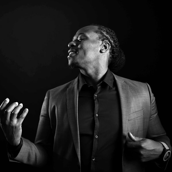 Femi Temowo poses as if with a guitar in his hands, lit from the side.