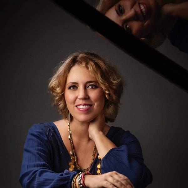 A woman smiles for camera, leaning across the top of a piano.