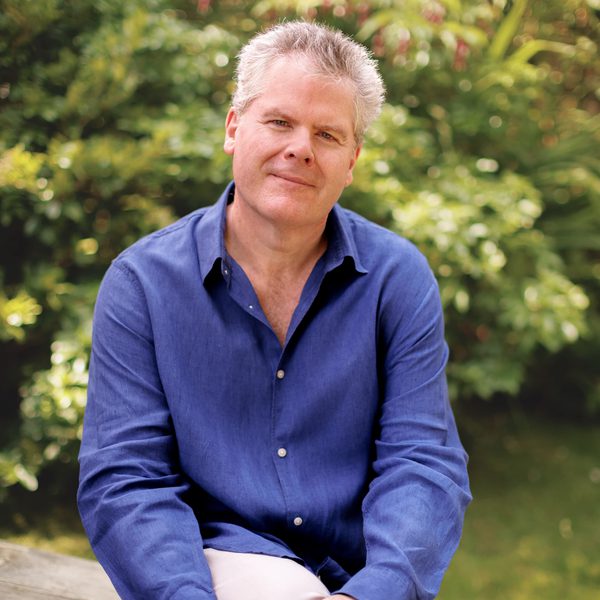 Gavin Carr sits on a bench looking to camera with hands clasped around one knee