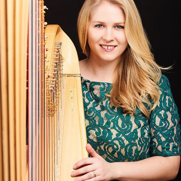 Portrait of Gwenllian Llŷr standing next to a harp, smiling to camera