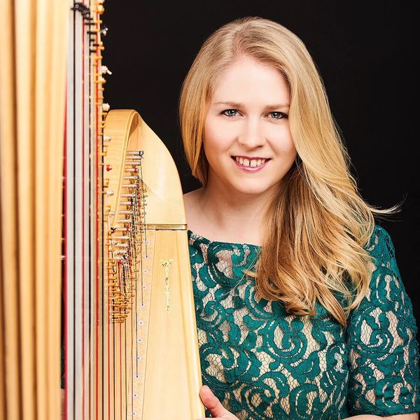 Portrait of Gwenllian Llŷr standing next to a harp, smiling to camera.