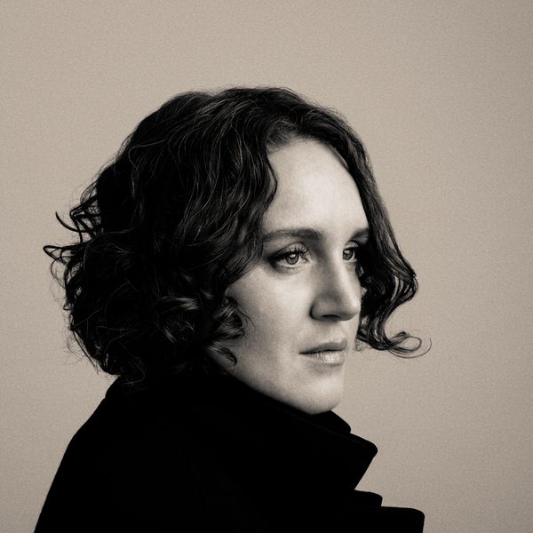 Profile photograph in monochrome of a lady with shoulder length dark wavy hair in a high collared jacket, looking off-camera.