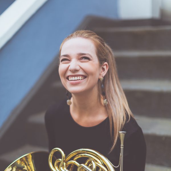 Portrait of Helen Kuby sitting on steps, holding a horn and smiling.
