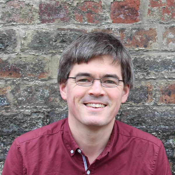 Huw Daniel smiles to camera, against a brick wall.