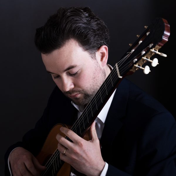 A classical guitarist performs and looks down pensively.