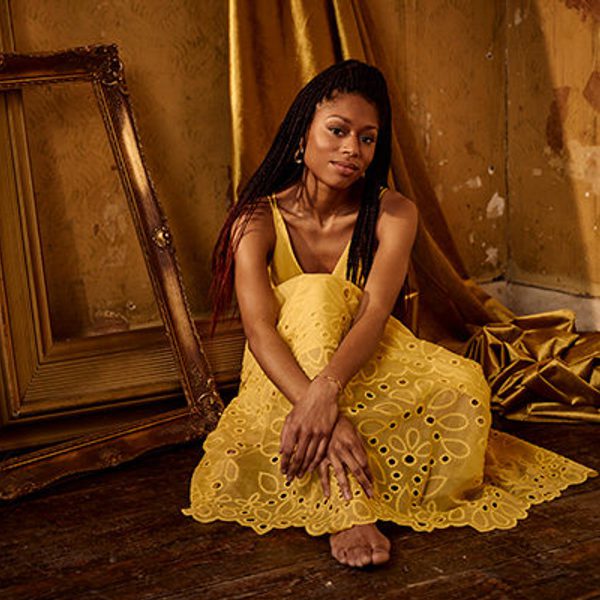Pianist Isata Kanneh-Mason kneels in a bright dress, looking to camera.