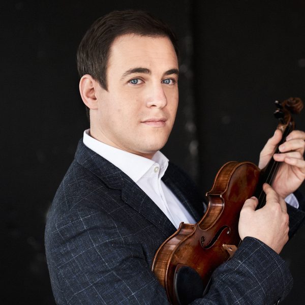 Jack liebeck smiles to camera, holding violin.
