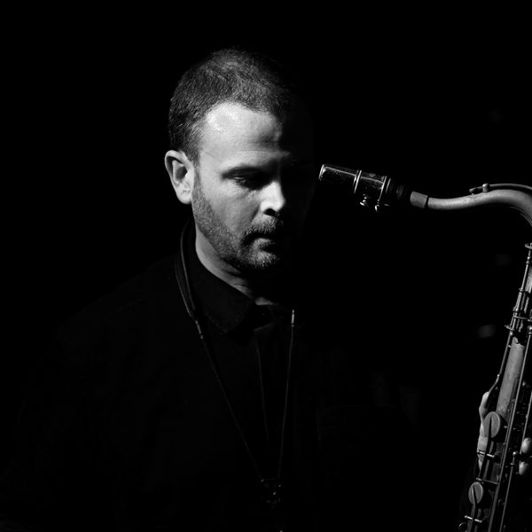 James Allsopp looks downwards and holds a saxophone.