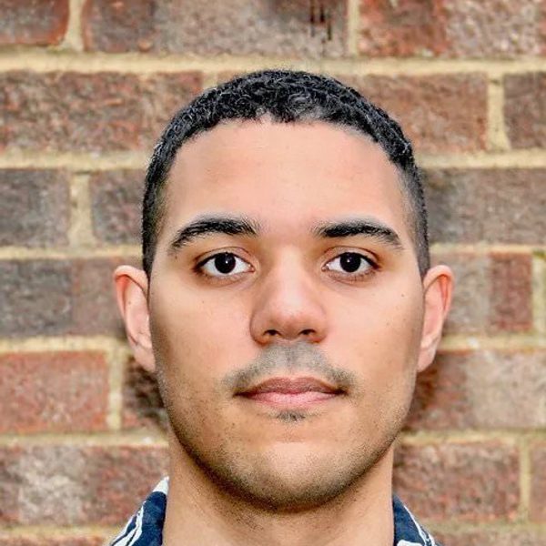 James B Wilson looking to camera against a brick wall.