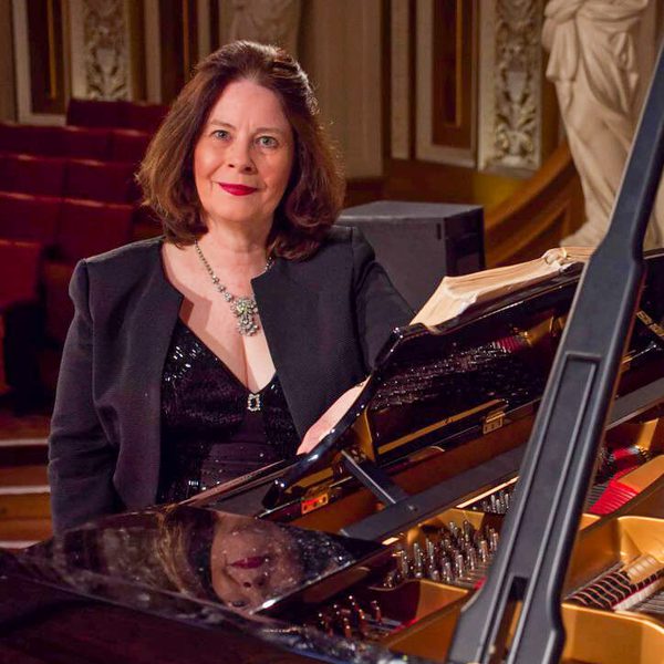 Janet Haney sits at a piano, facing camera.