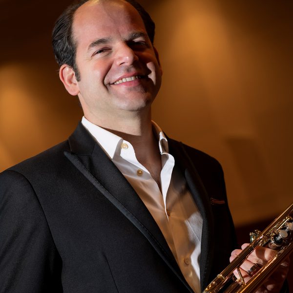 Jeroen Berwaerts smiles to camera holding a trumpet.