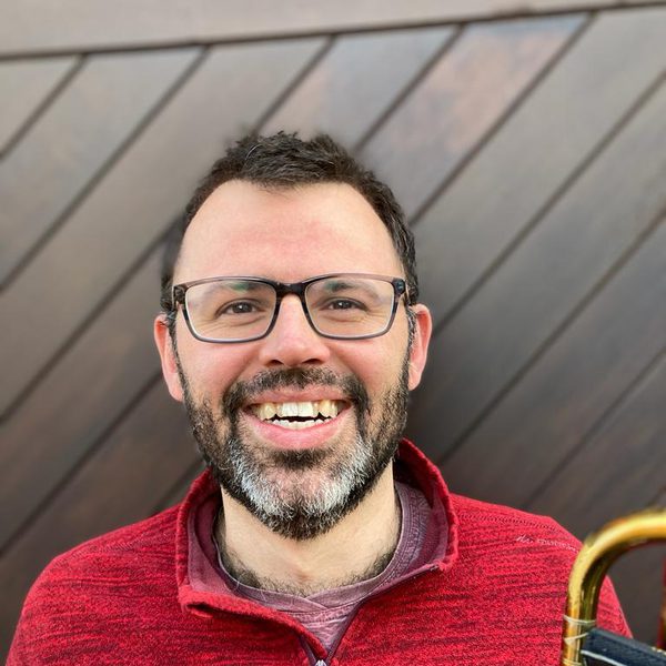 Jim Maynard smiles to camera while holding a trumpet.